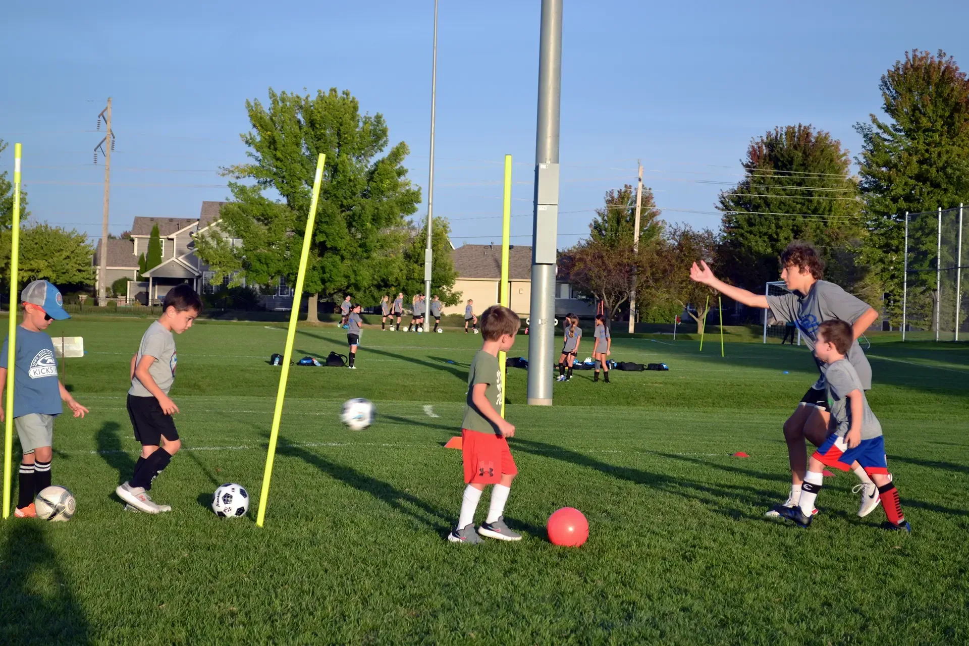 Children playing soccer on a grassy field with training poles on a sunny day