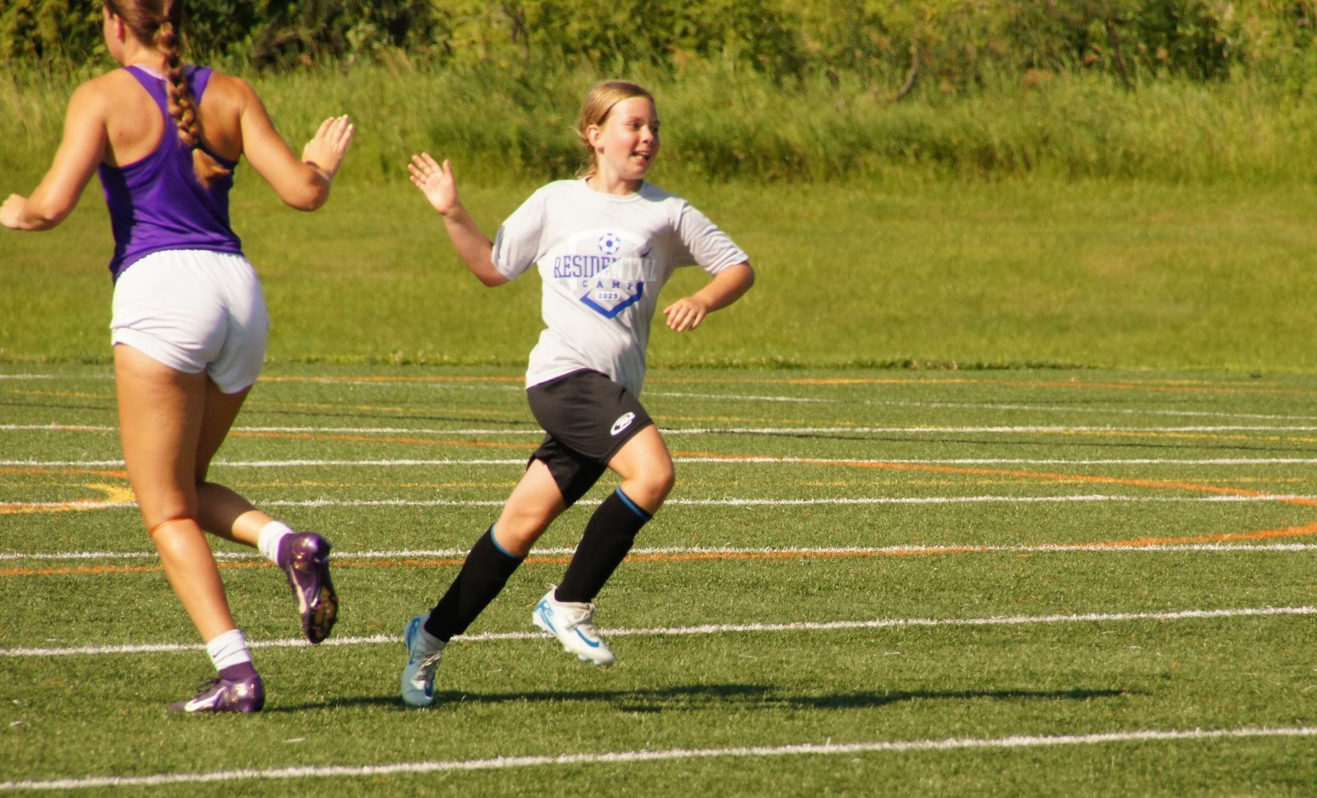 Two runners on a grassy track, one in purple and white, one in white and black, mid-race