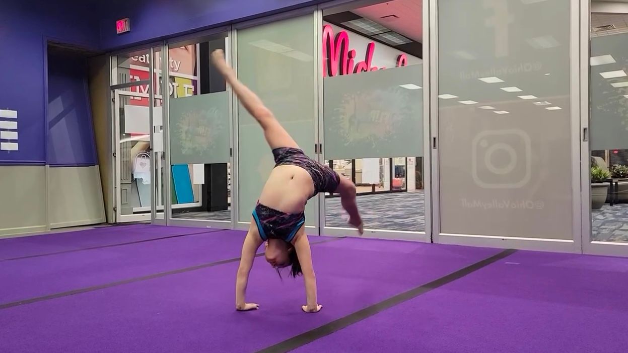 A young girl is doing a handstand on a purple mat in a gym.