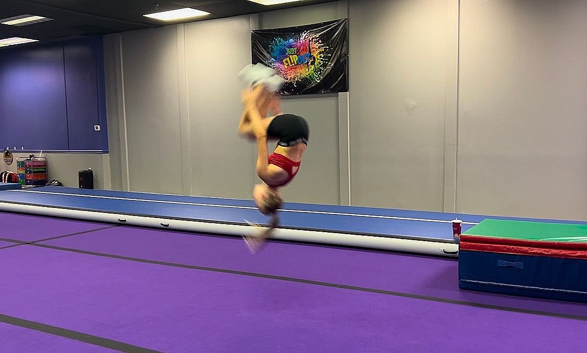 A person is jumping in the air on a trampoline in a gym.