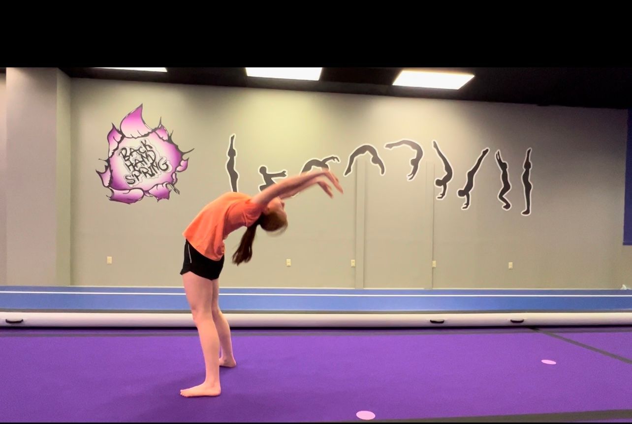 A girl is doing a handstand on a purple mat in a gym.