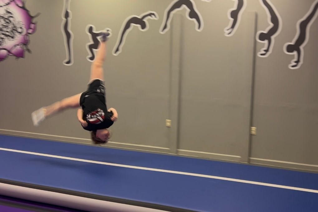 A person is doing a handstand on a mat in a gym.