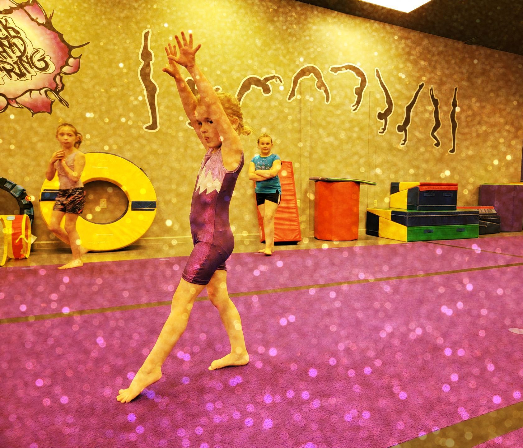 A girl is standing on a purple mat in a gym