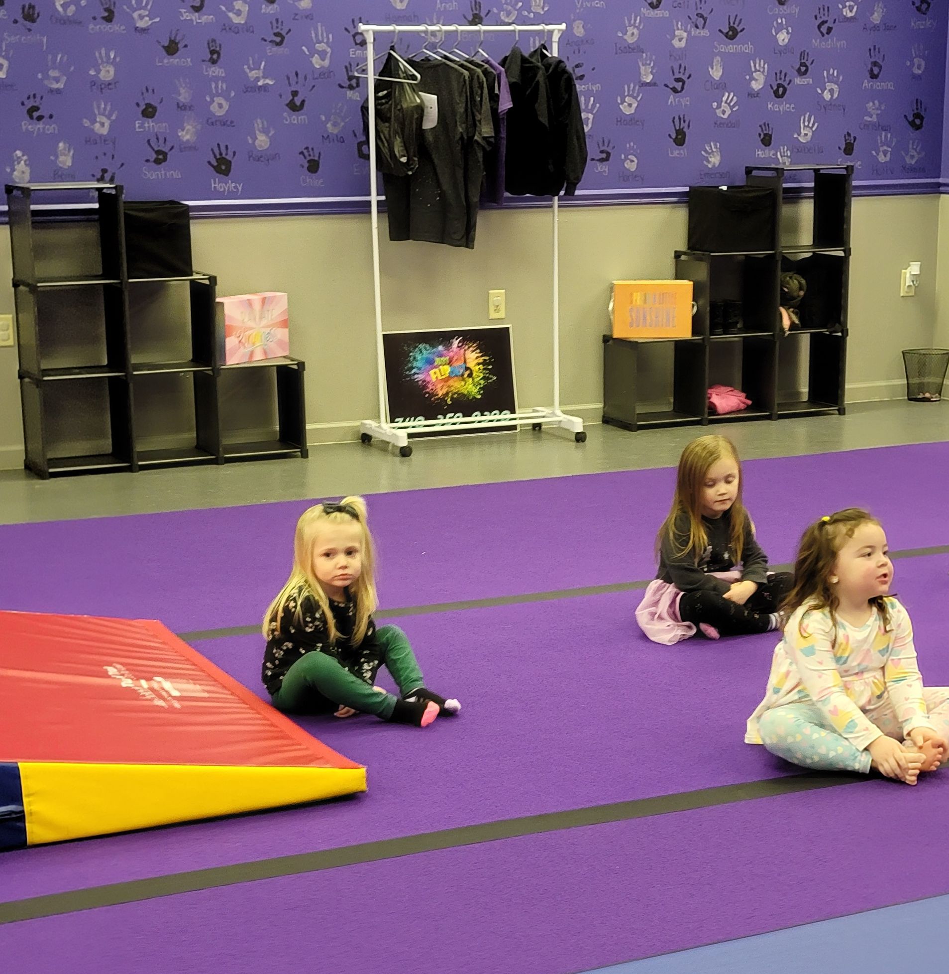 Three little girls are sitting on a purple mat in a gym