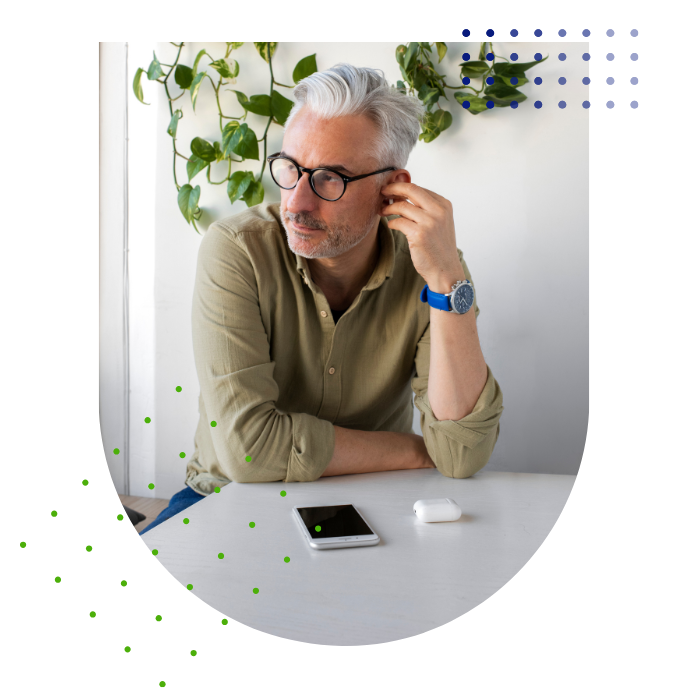 A man wearing glasses is sitting at a table with a cell phone.