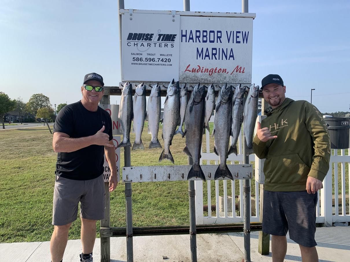 Two men are standing in front of a sign that says harbor view marina.