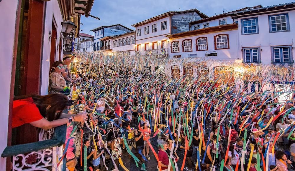 Uma mulher está em uma sacada observando uma multidão de pessoas no carnaval de rua em Diamantina/MG