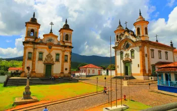 Igrejas com duas torres dispostas uma ao lado da outra em um campo verdejante na cidade de Mariana.