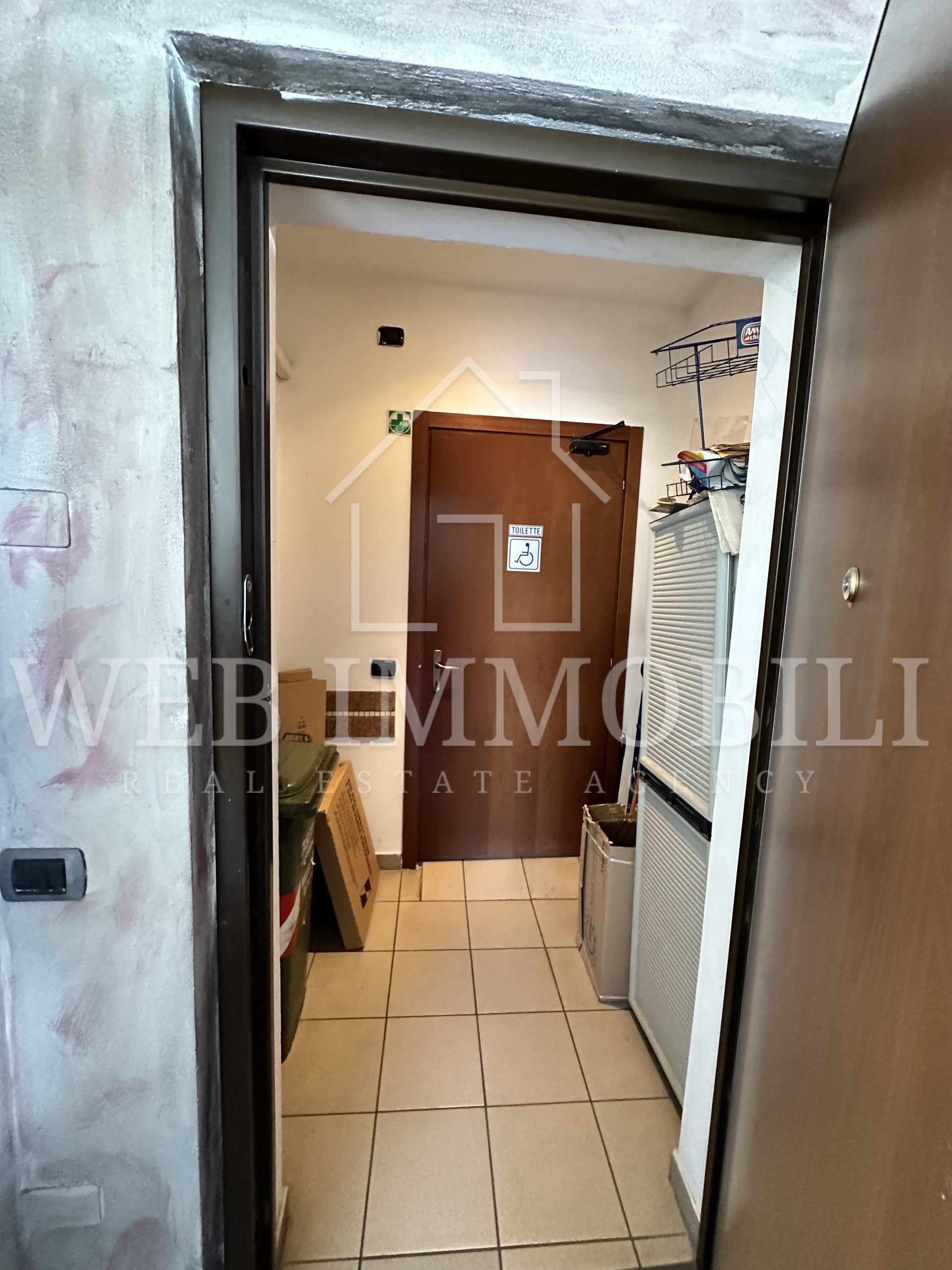 Porta interna che dà su un corridoio con una porta marrone chiusa, pavimento piastrellato e vari oggetti.