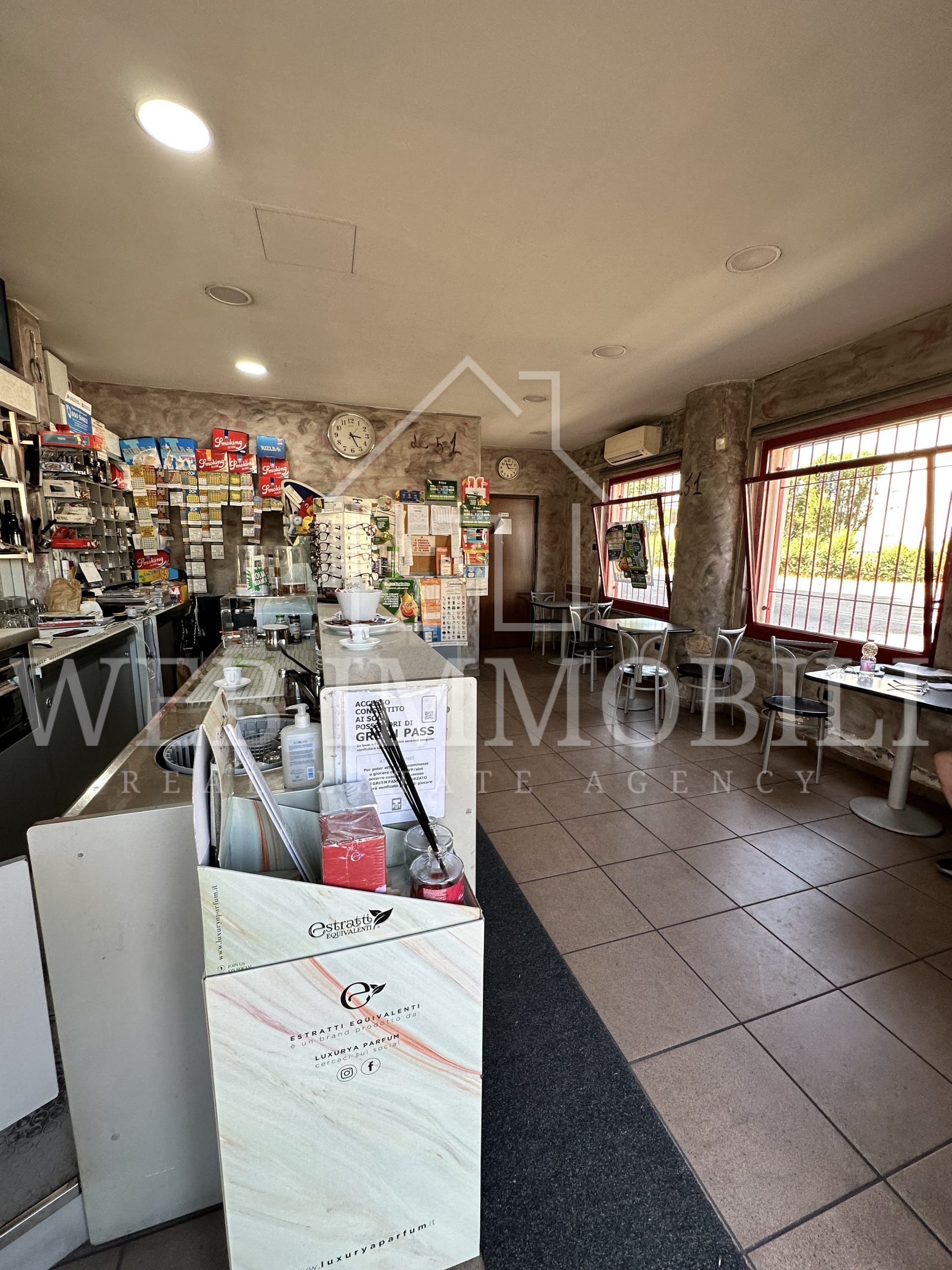 Interno di un bar con bancone, tavoli e sedie.