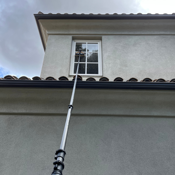 Telescoping pole reaching a second-story window on a gray stucco house