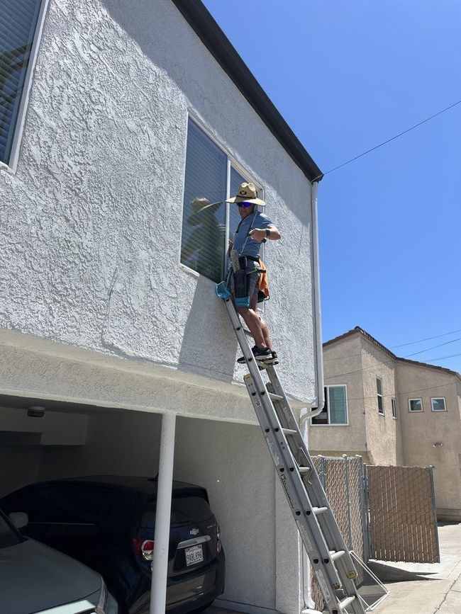 Worker on ladder painting the exterior wall of a two-story house.