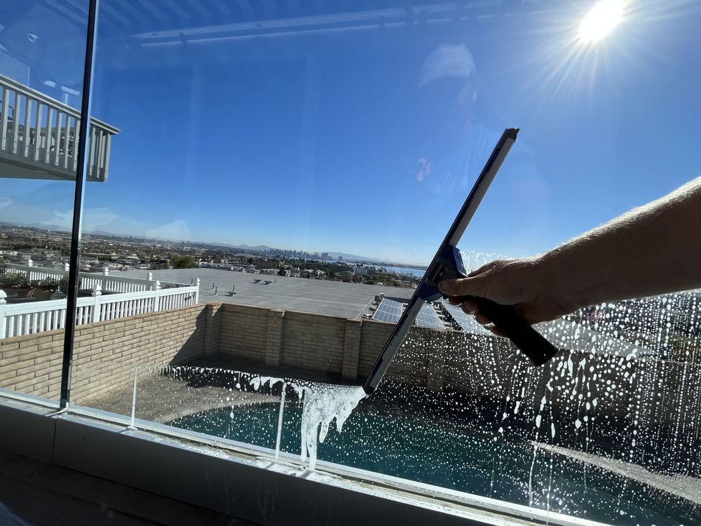 Person cleaning a sunlit rooftop pool with a squeegee, mountains in the distance