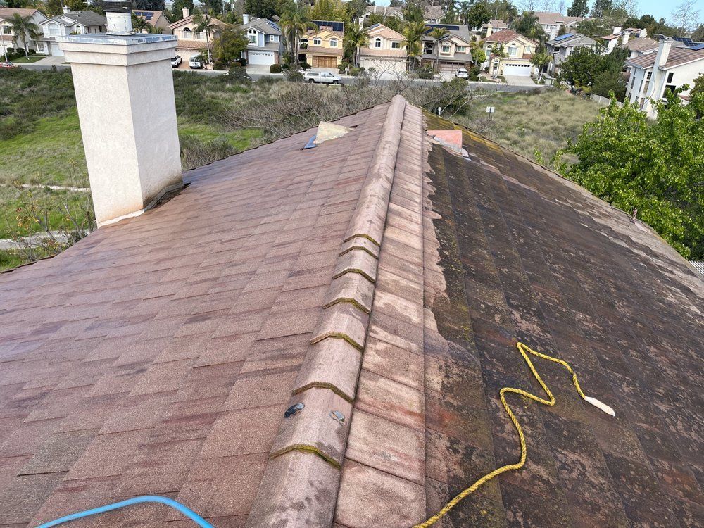 Roof ridge with pink tiles and dark weathered shingles, viewed from above with houses and trees in the background