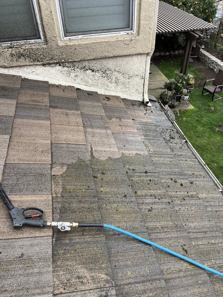 Rooftop shingle repair area with a hose and a power tool near a house wall, showing weathered patches.