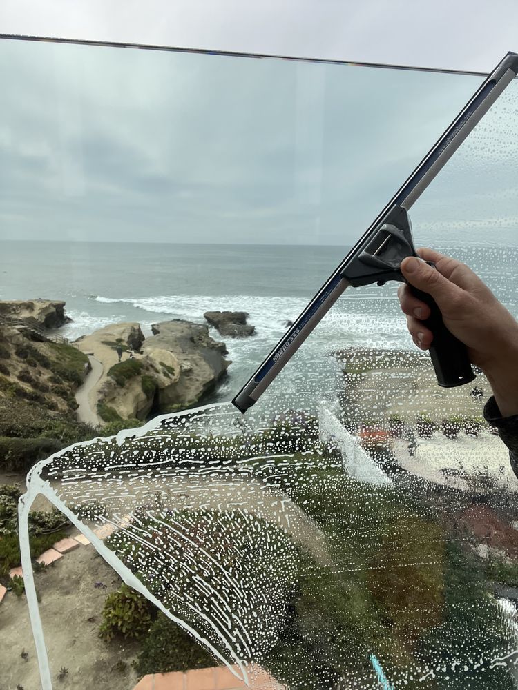Windshield being cleaned with a squeegee overlooking a cloudy ocean cliffside.