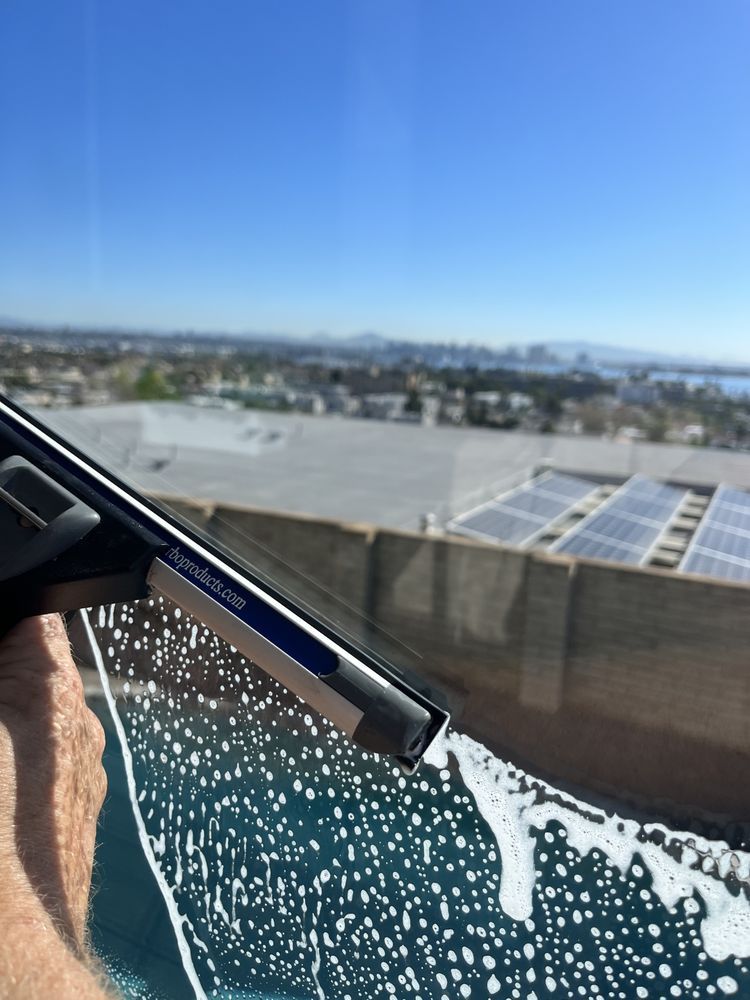 Windshield wiper spraying water on a car windshield with a sunny city skyline in the background
