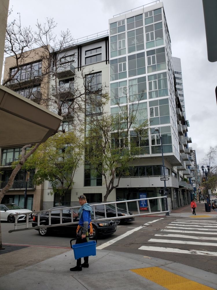 Urban street corner with a modern glass building and a person walking with a blue cart