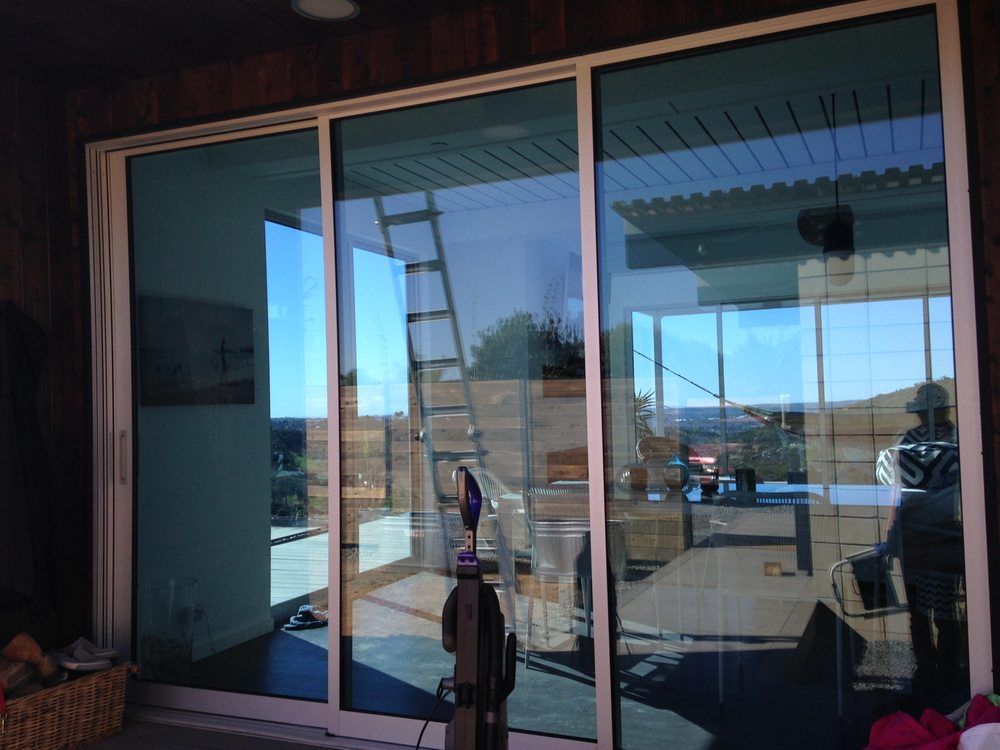 Sliding glass doors reflecting a sunny patio and outdoor deck with railing and ladder.