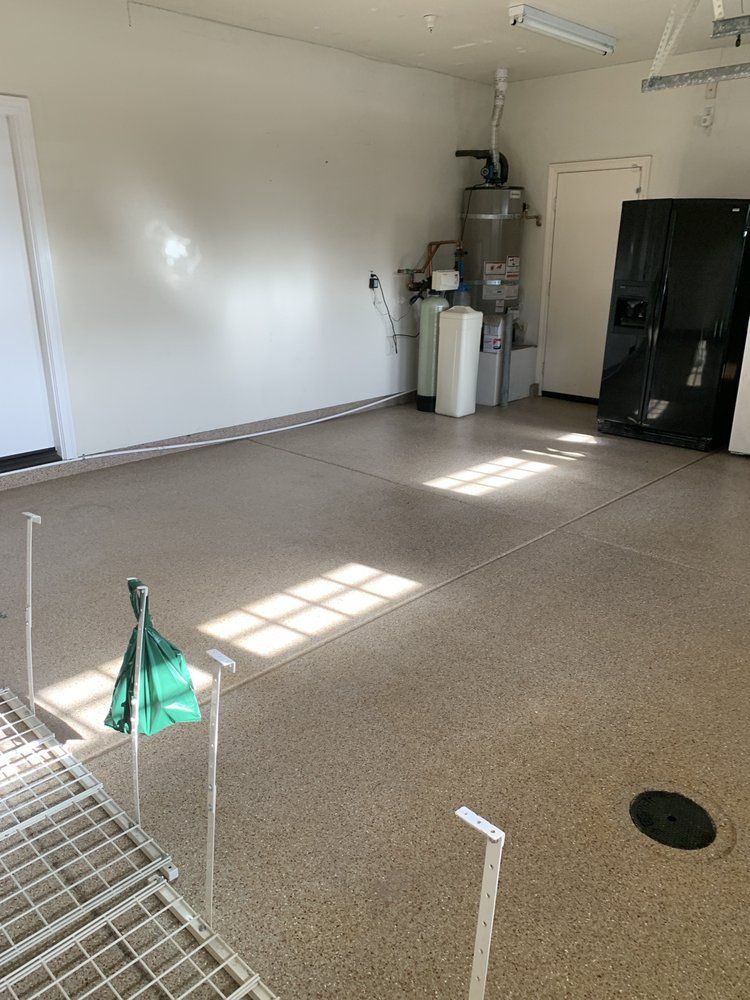 Empty garage interior with white walls, black cabinet, and sunlight on speckled floor.