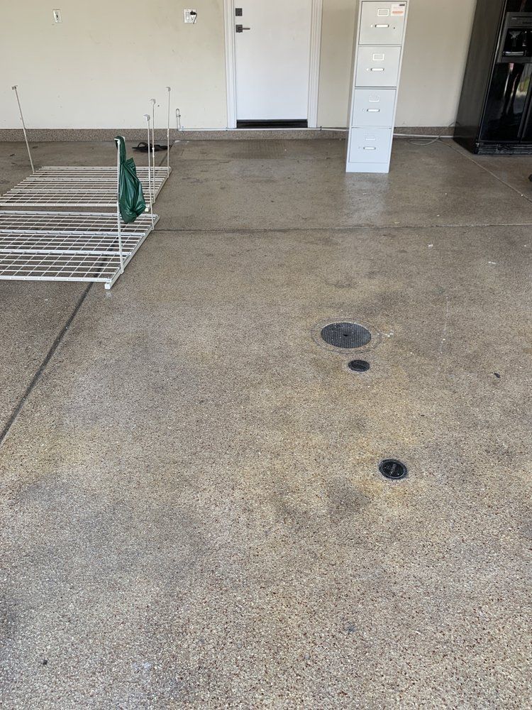 Concrete garage floor with several dark circular stains and a metal rack near the wall