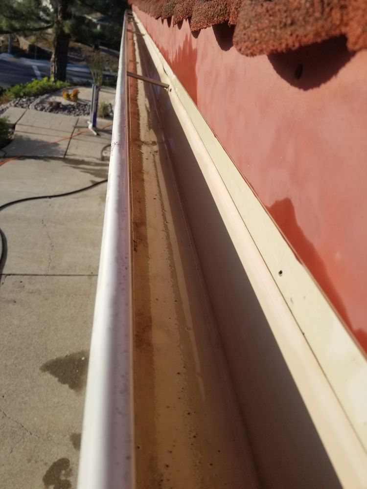 White gutter along a pink exterior wall beside a concrete walkway and garden.