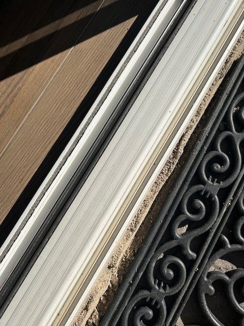 Close-up of a dirty window frame beside a black metal railing and tiled wall.
