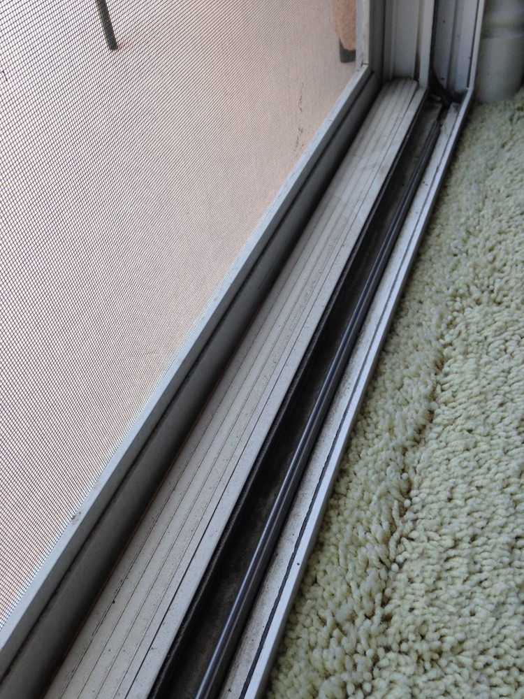 Window track beside a textured screen, with carpet and metal frame close-up.