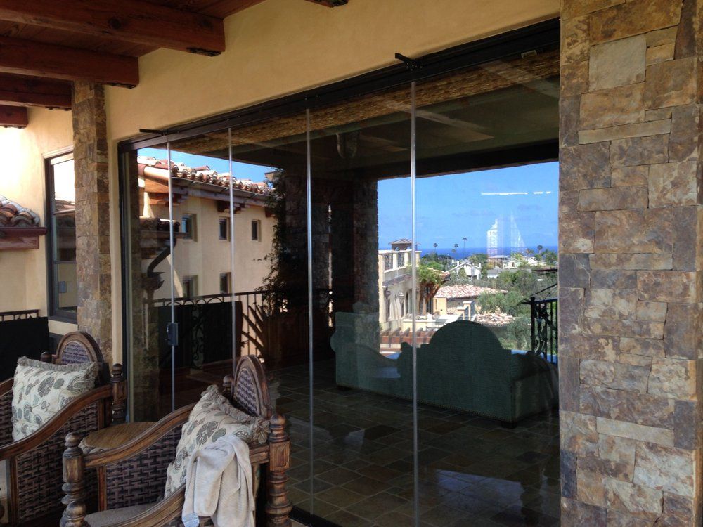 Covered patio with wicker chairs, large glass sliding doors, and a view of the seaside village outside
