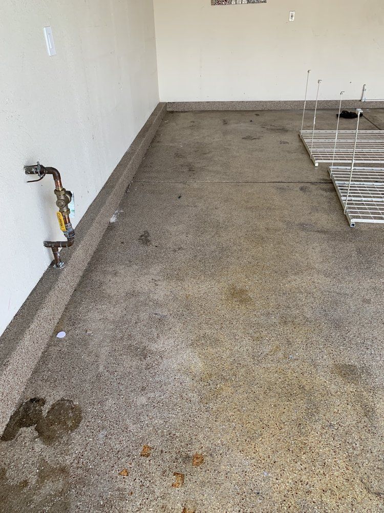 Empty concrete utility room with exposed plumbing and a metal rack on the right