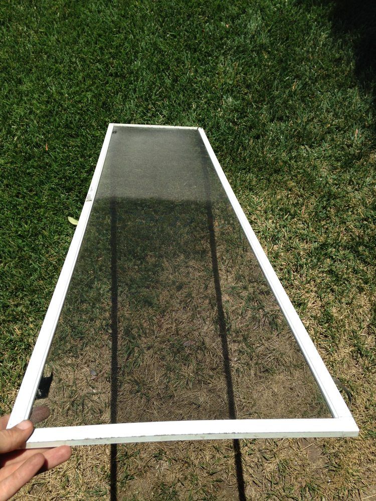 Hand holding a rectangular mesh screen with white frame against grass background