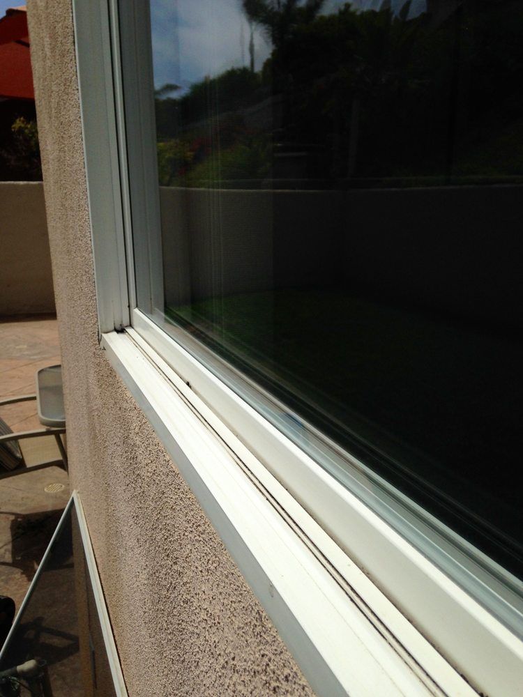 Close-up of a white window frame and sill beside a tan stucco wall, with dark reflective glass.