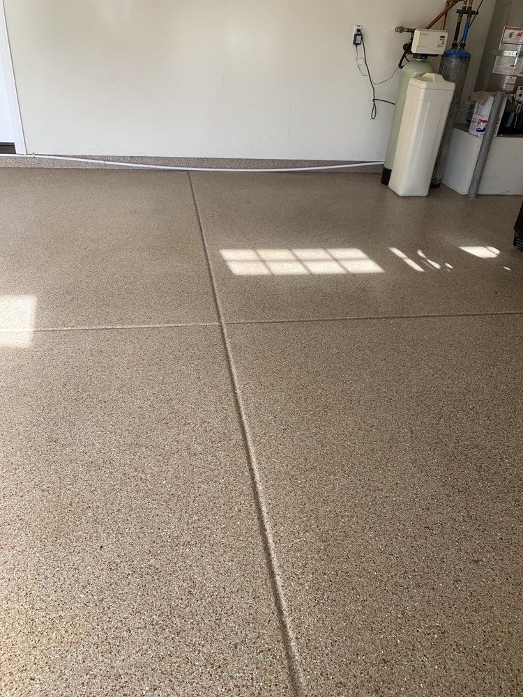Empty garage with tan floor, white wall, and sunlight casting window shadows.