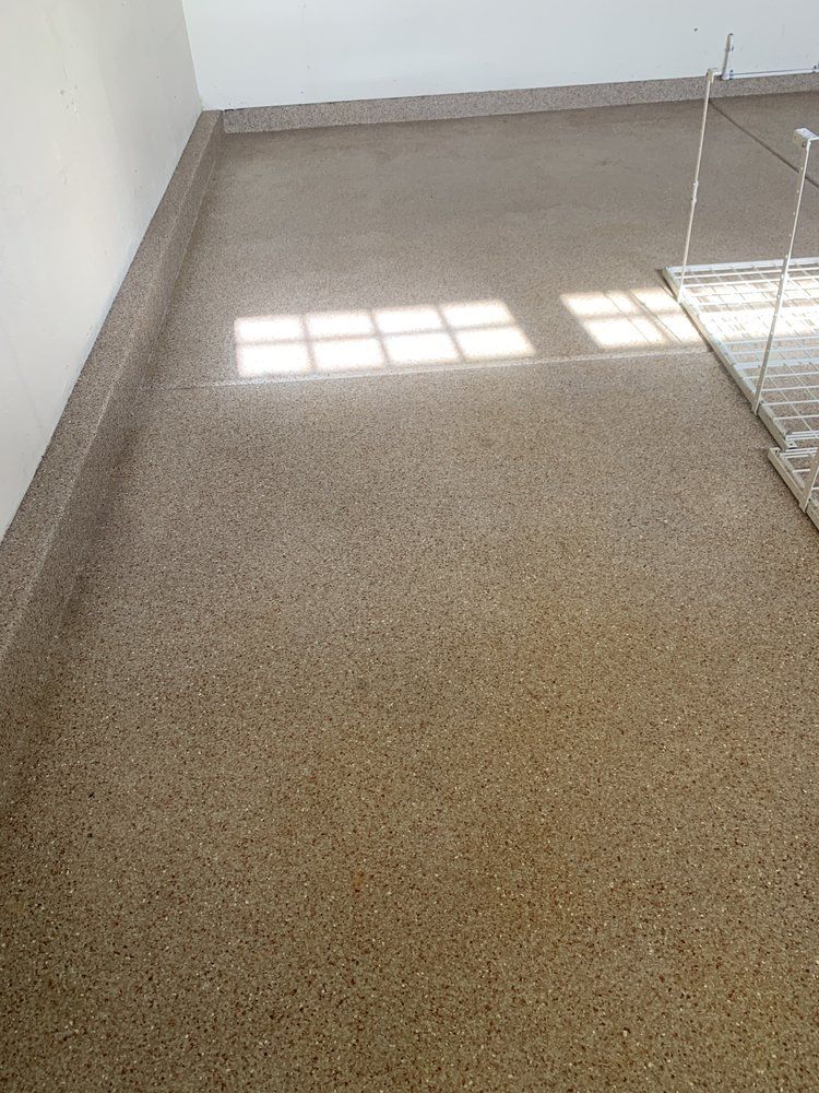 Empty beige room with sunlight on a speckled floor and a drying rack at the right edge