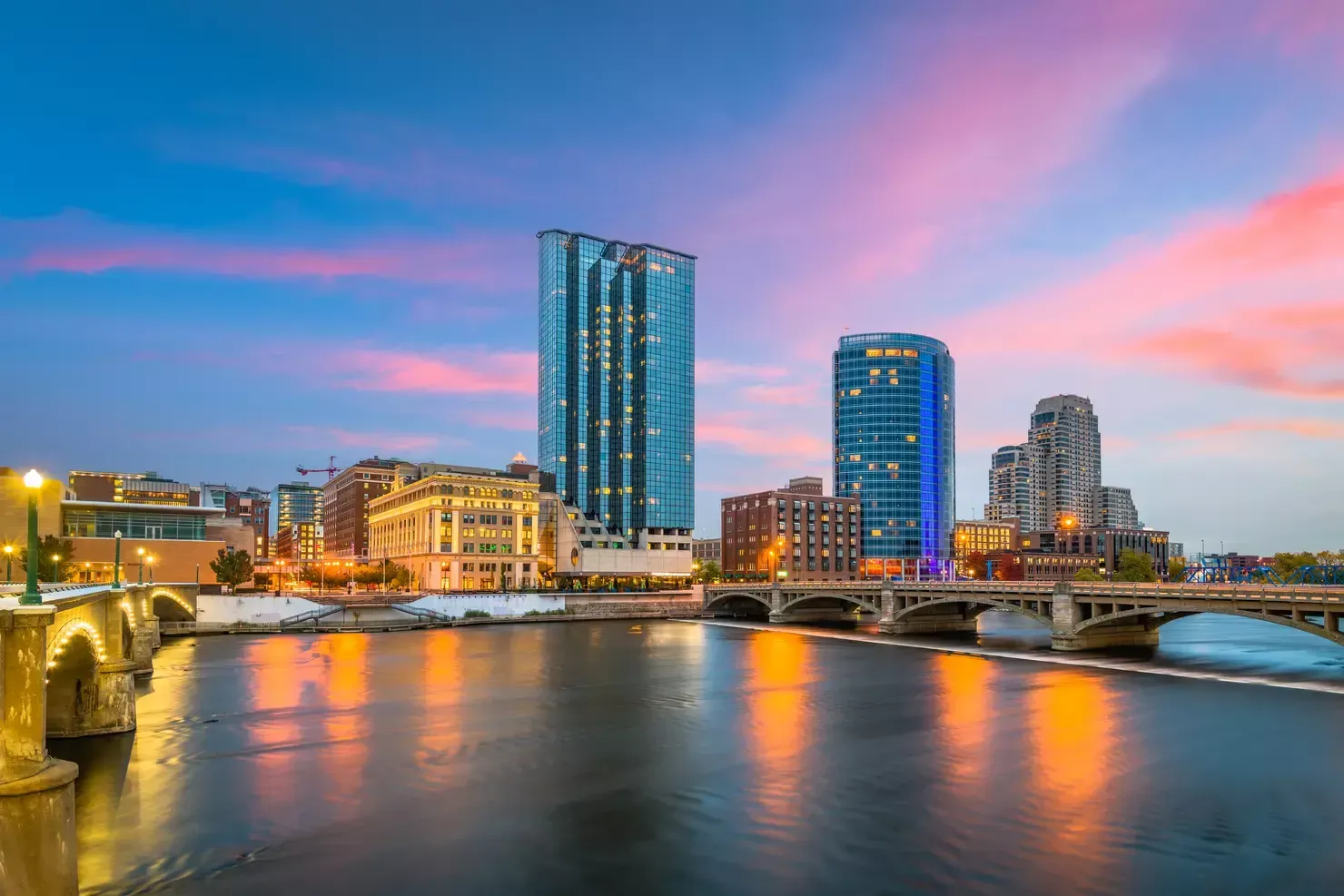 A city skyline with a bridge over a river at sunset.