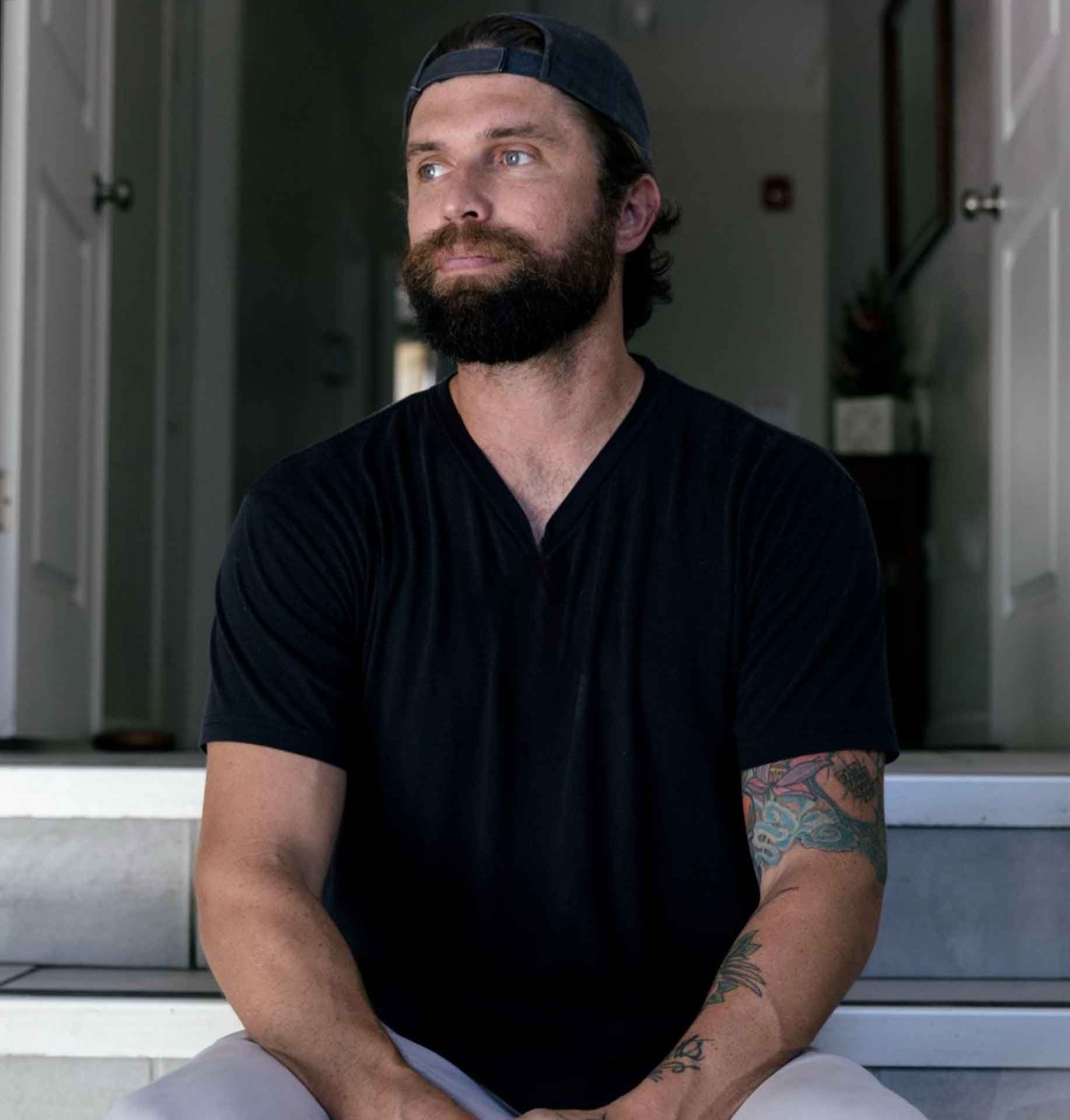 A man with a beard wearing a baseball cap and a black shirt