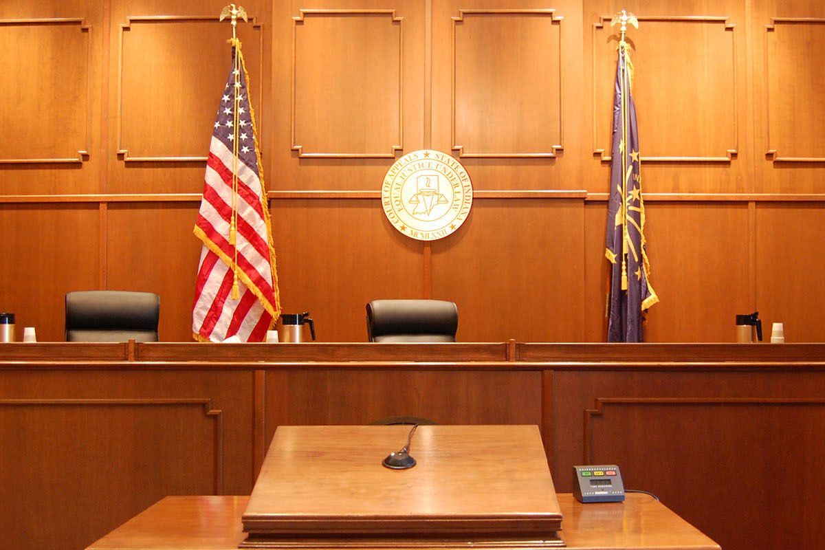 A judge 's bench in a courtroom with flags on the wall.