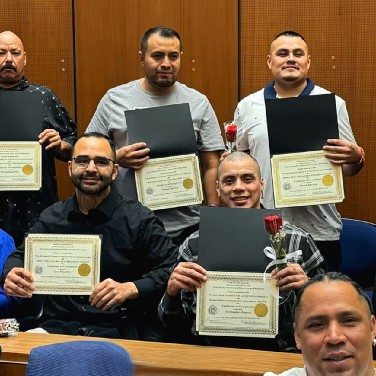A group of men are holding certificates and a rose