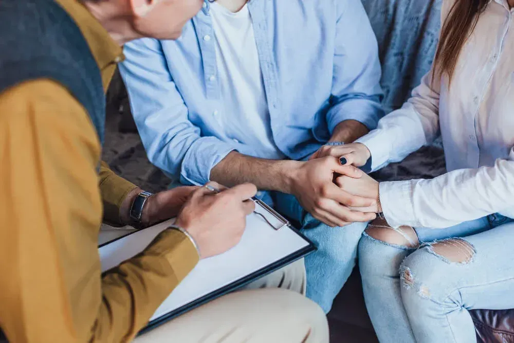 A group of people are holding hands while a man writes on a clipboard.