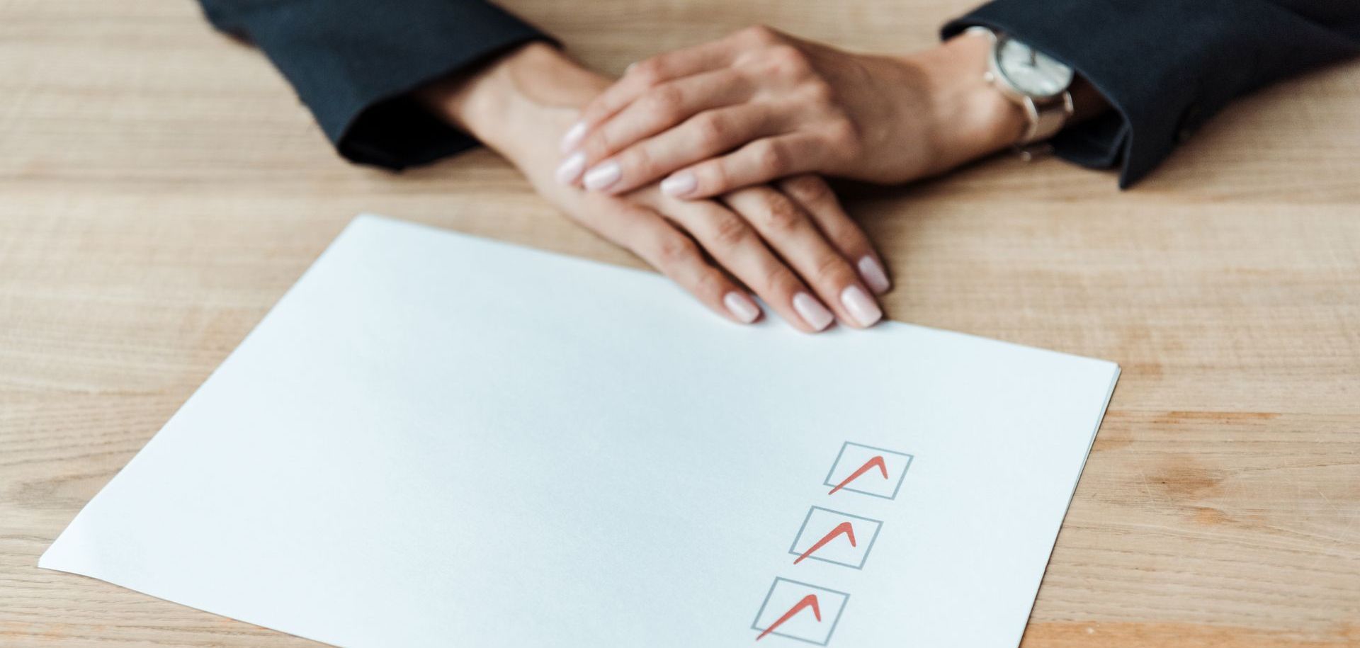 A woman is sitting at a table with her hands folded over an envelope with check marks on it.