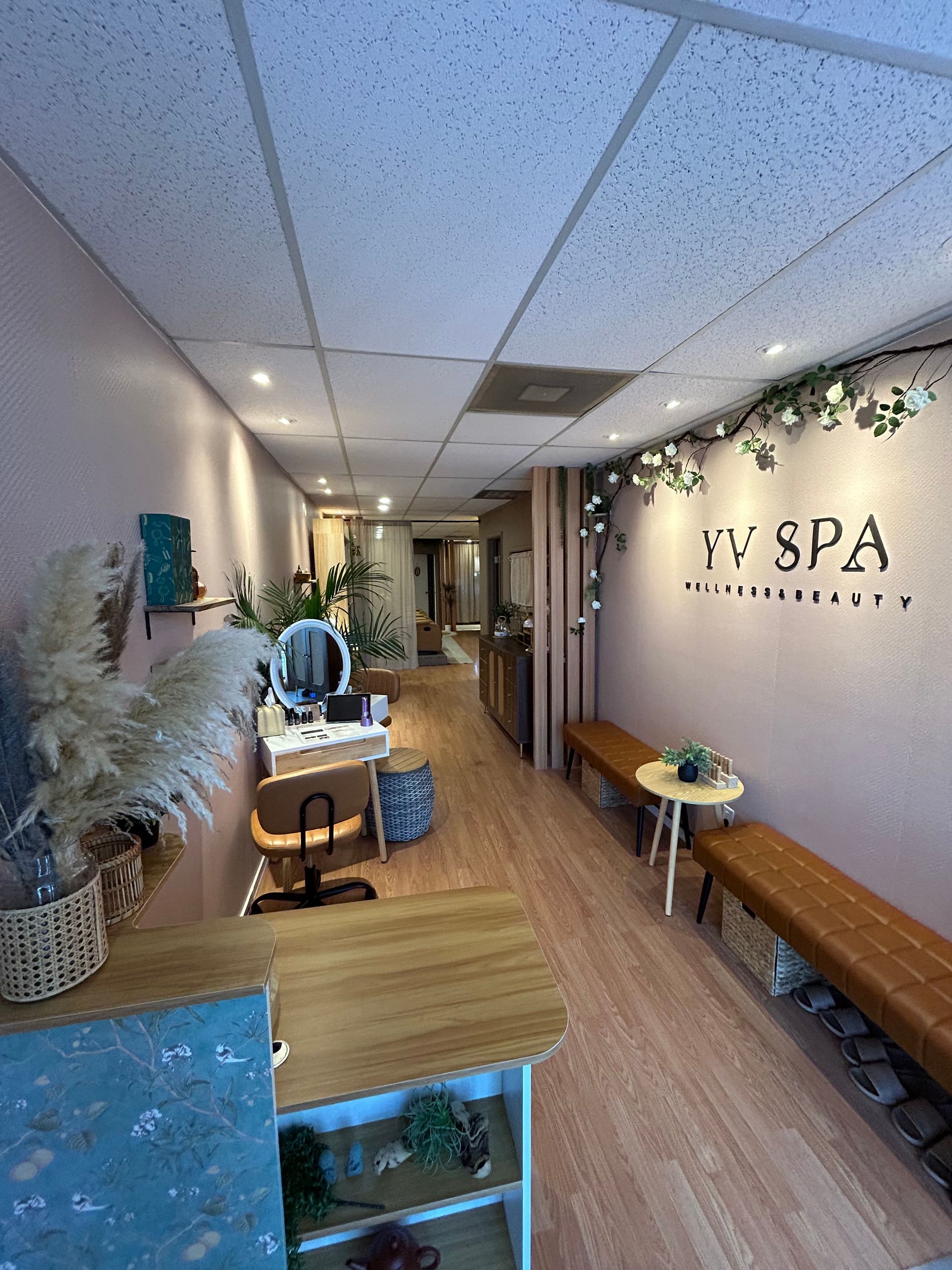 Interior of a spa with pink walls, wood floors, and benches. Reception desk and plants are visible.