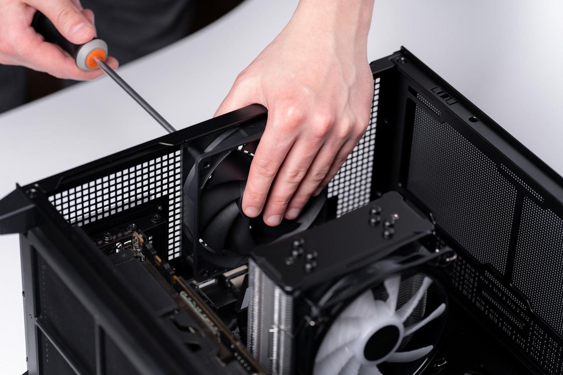 Person installing a computer fan into a black computer case with a screwdriver.