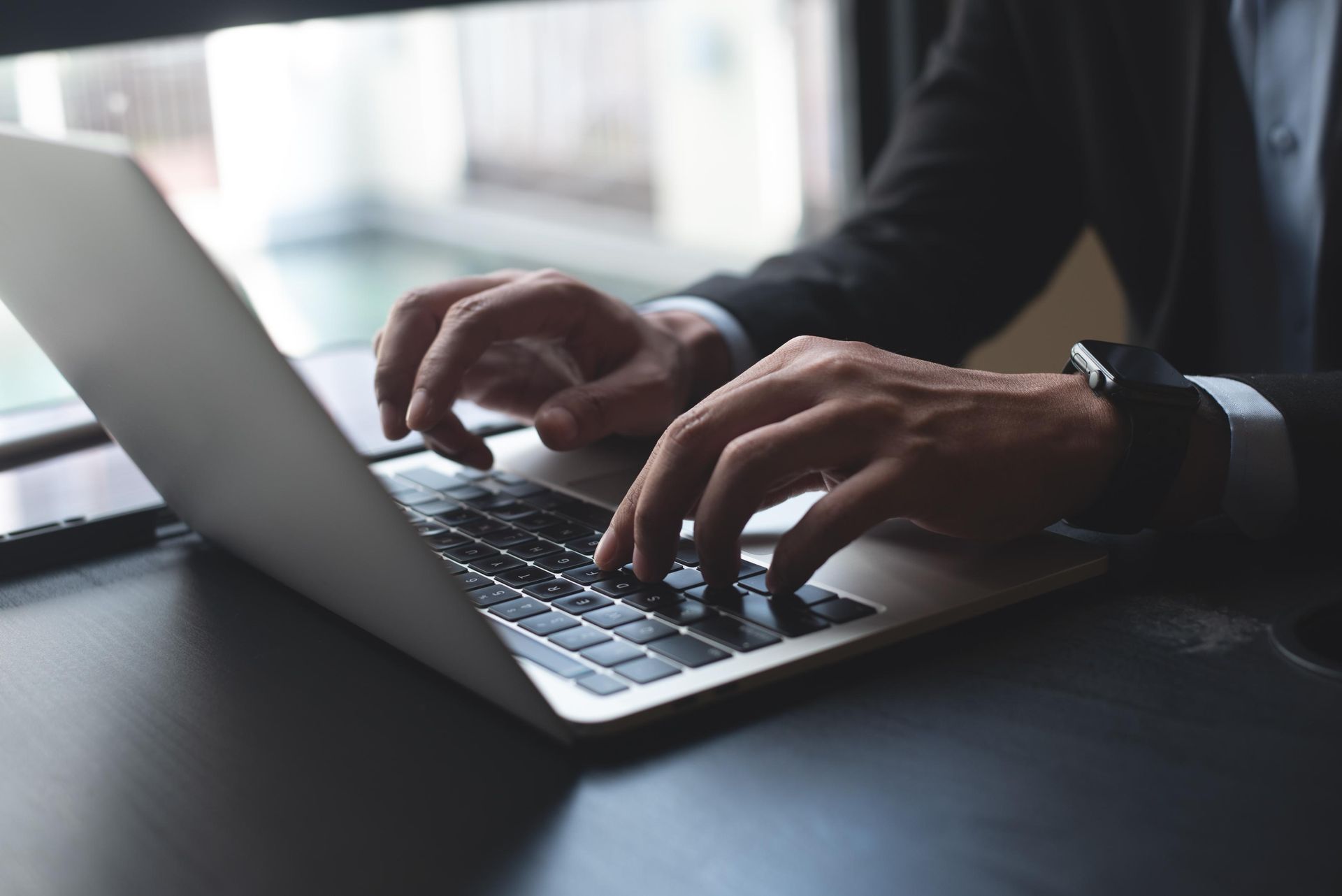 Person in suit typing on a laptop at a desk.