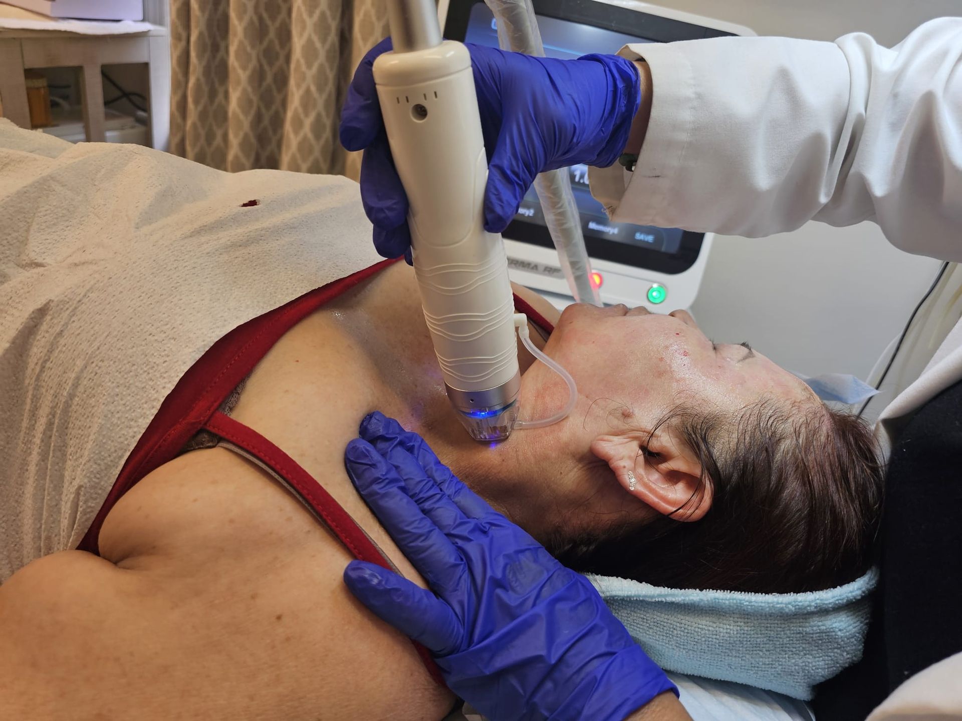 A person receiving a facial treatment. A medical professional holds a device near the face and neck.