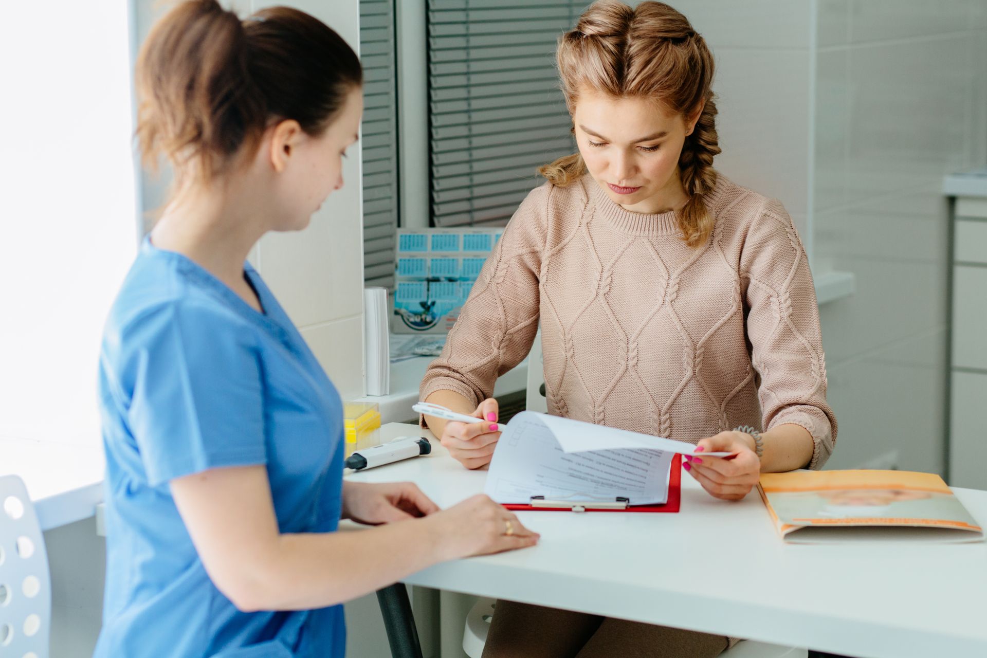 Woman reviewing paperwork with a nurse in a medical office; both are looking at the document.