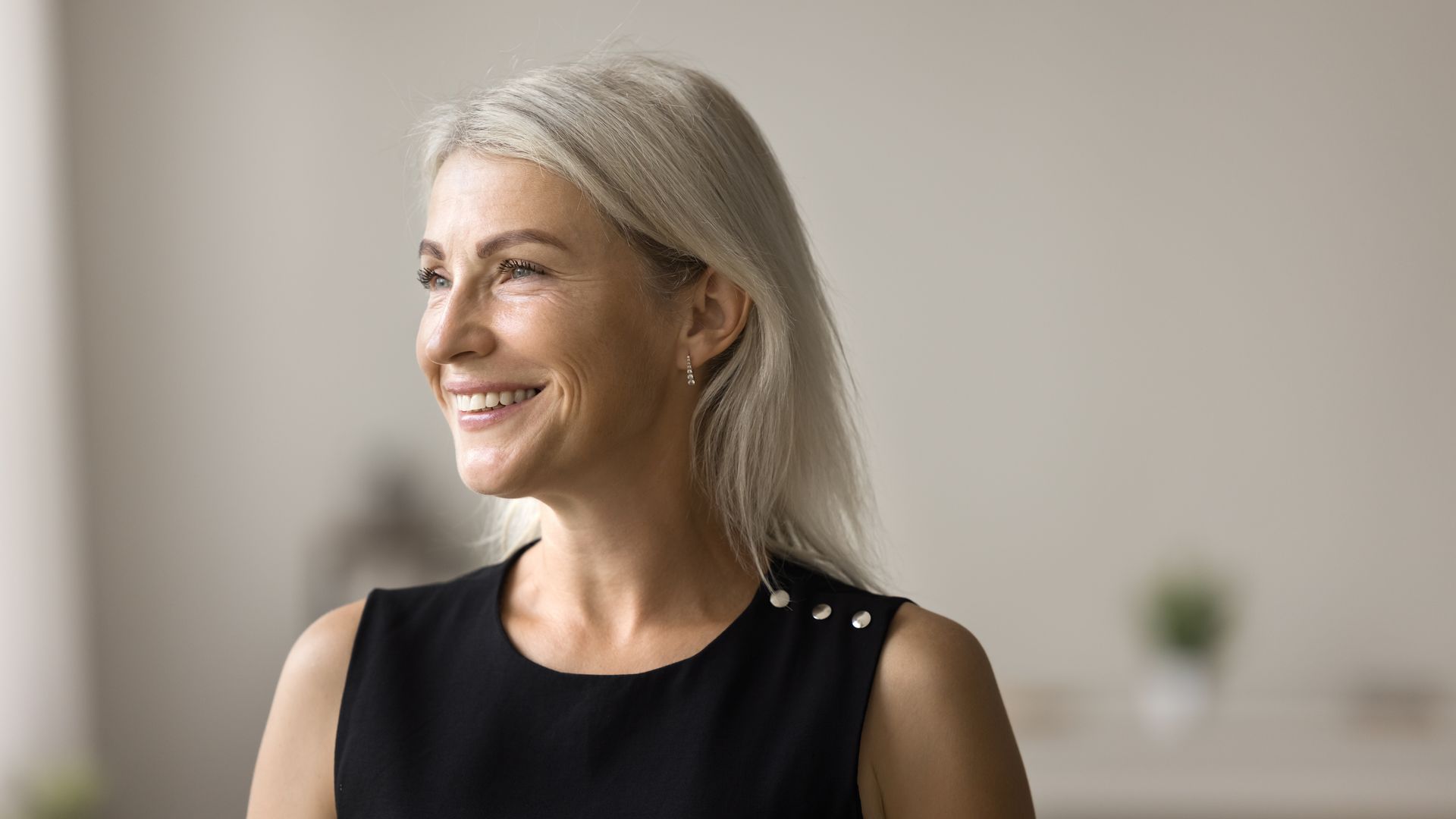 A woman with gray hair is wearing a black dress and smiling.