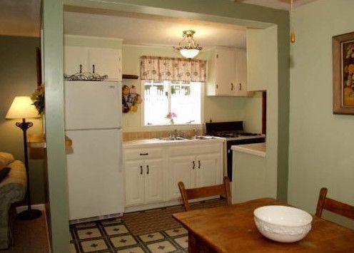 Bright modern white kitchen with island, pendant light, stainless fridge, and large windows