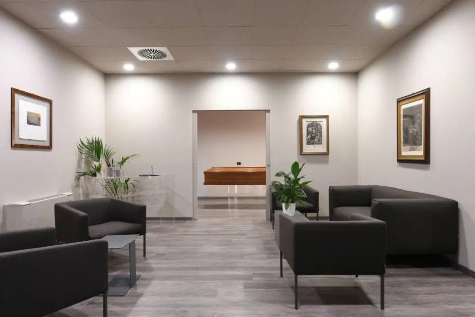 Sala d'attesa moderna per ufficio con divani neri, sedie grigie, piante in vaso e illuminazione a incasso.