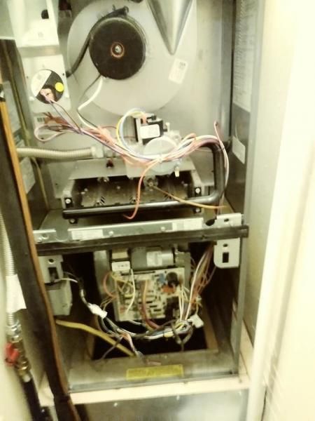 An open residential gas furnace with an exposed interior featuring wiring, a circular blower, and a circuit board.