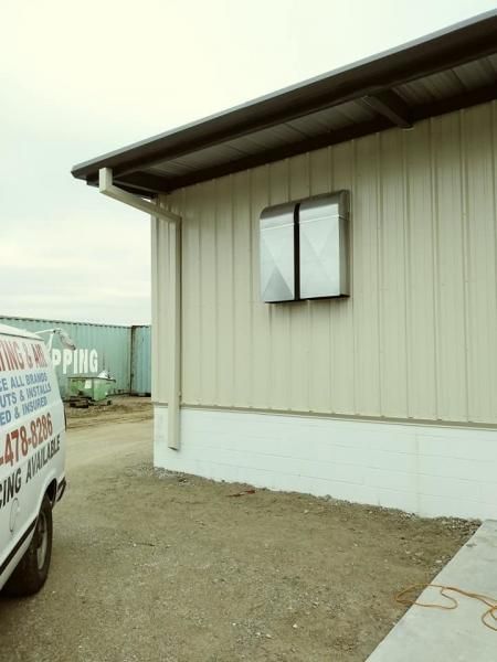 Side view of a beige metal building with a gutter and a wall-mounted unit next to a white service van.